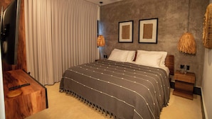 Une chambre à coucher avec un grand lit, une télévision, un ventilateur de plafond et deux œuvres d’art encadrées accrochées au mur.