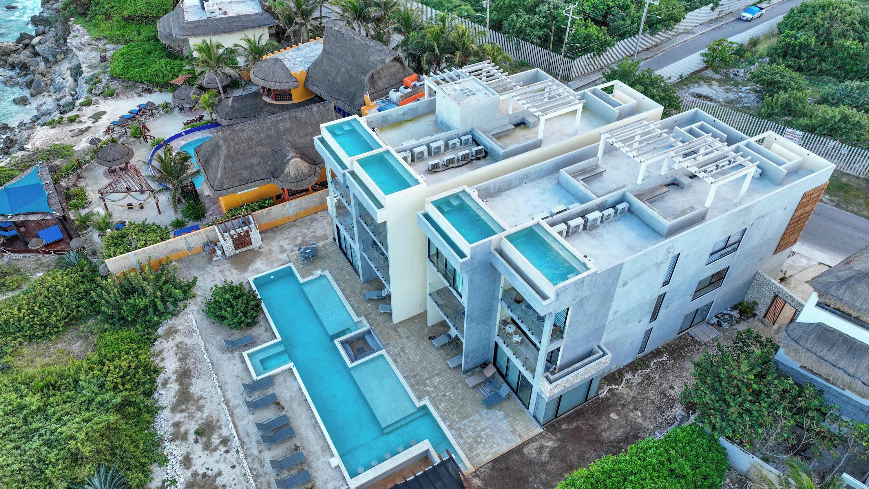 A modern hotel with multiple swimming pools, a rooftop pool, and a beach area with umbrellas.
