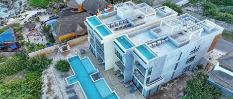 A modern hotel with multiple swimming pools, a rooftop pool, and a beach area with umbrellas.