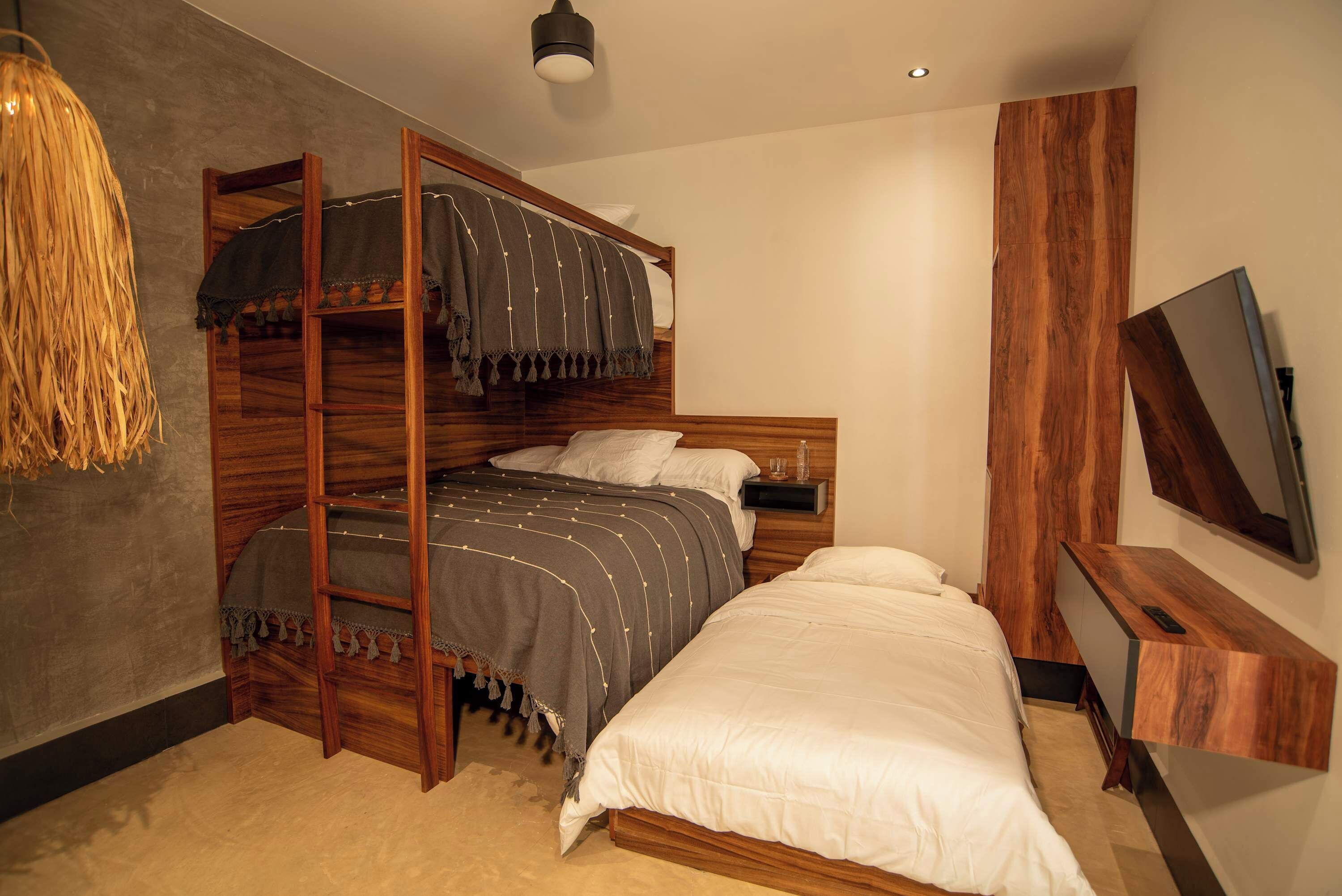 Un dormitorio con una litera, una mesita de noche, un televisor y una lámpara colgante.