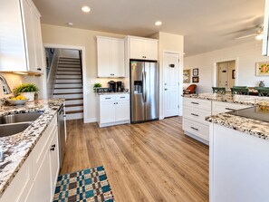 A modern kitchen with white cabinets, a stainless steel refrigerator, and a wooden floor. - Family-friendly Home Steps to Beach | Sleeps 12 (Gulf Shores)
