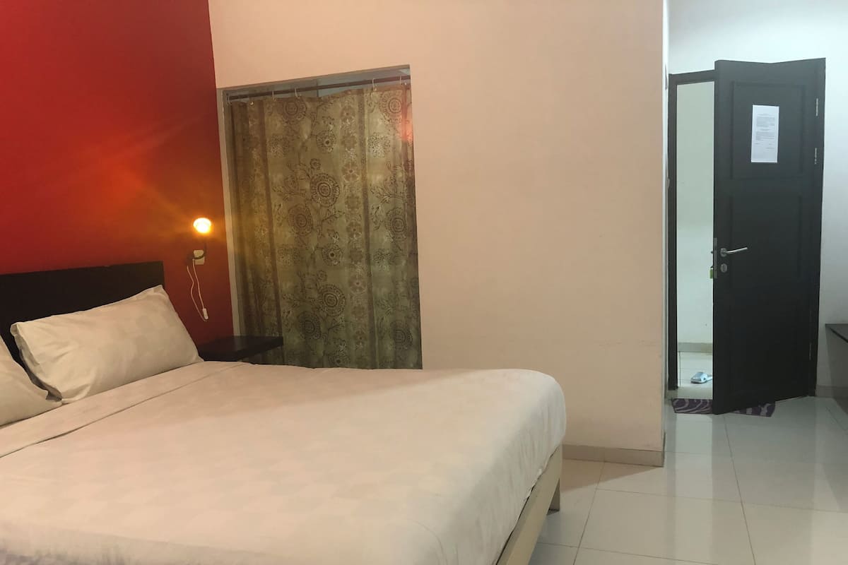 Quarto de hotel com cama, mesa de cabeceira, cortina e porta.