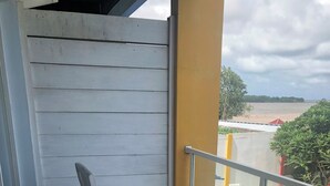 A balcony with a white table and chairs, a yellow pillar, and a view of the beach. - JEPARA BEACH HOTEL (Tahunan)