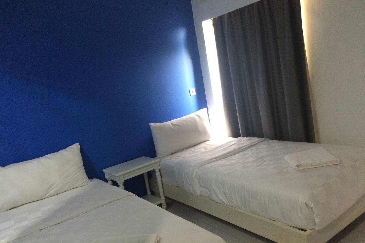 Quarto de hotel com duas camas, uma mesa de cabeceira e uma janela com cortinas.