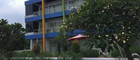 Un hotel de varios pisos con balcones, piscina y abundante vegetación.