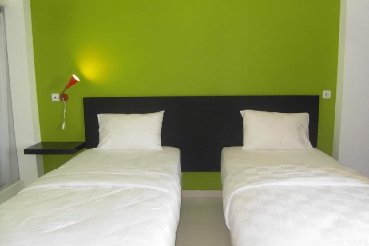 Quarto com duas camas, parede verde e luminária vermelha em uma mesinha de cabeceira.