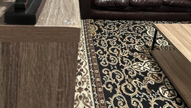 Un salon moderne avec un canapé en cuir marron foncé, un tapis à motifs et des œuvres d’art abstraites accrochées au mur.