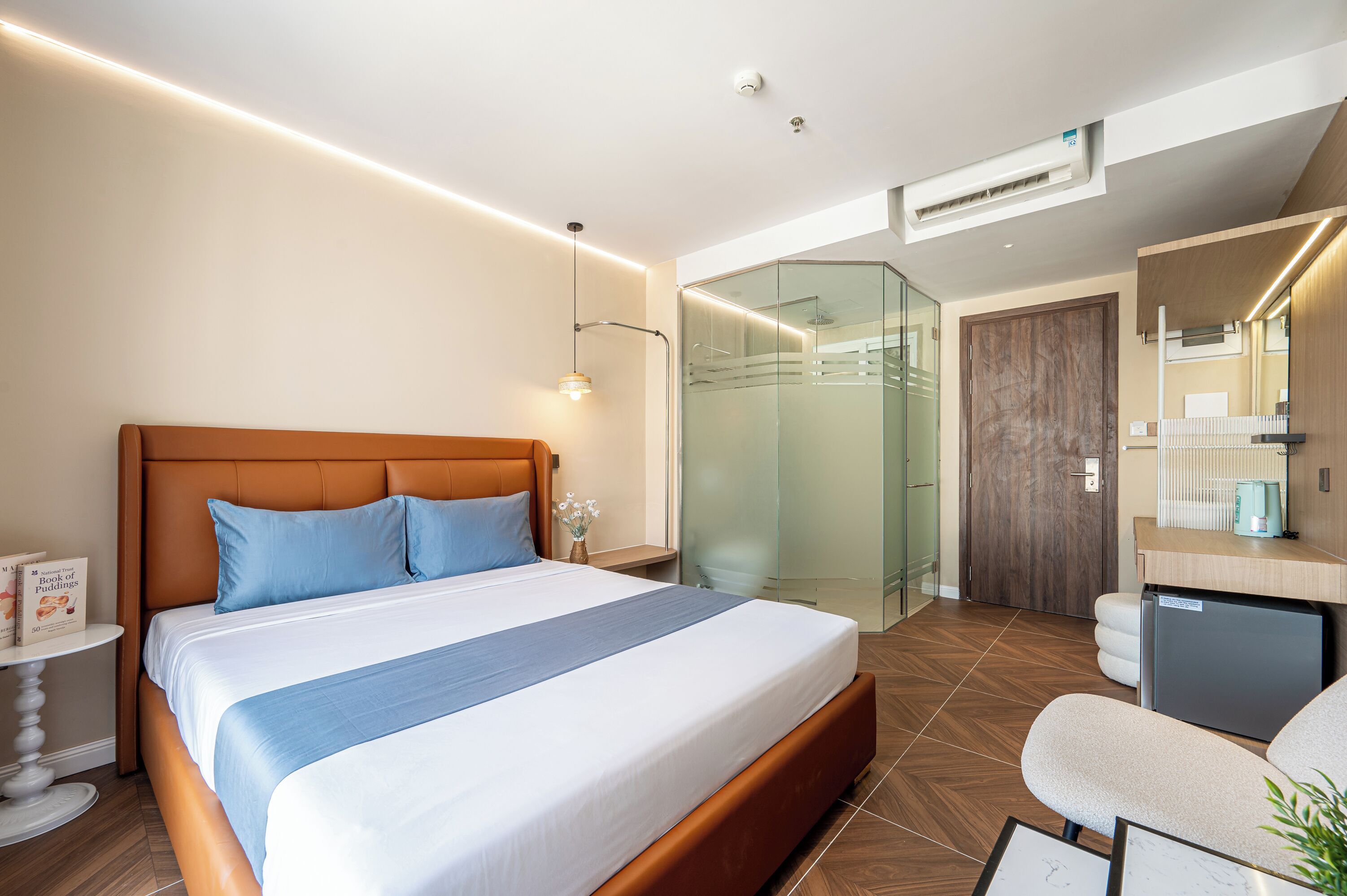 A modern hotel room with a large bed, a desk, a shower, and a small refrigerator.