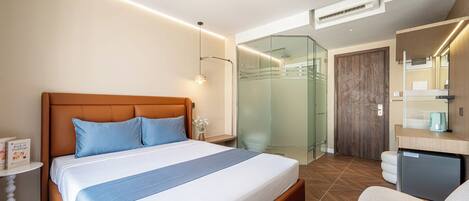 A modern hotel room with a large bed, a desk, a shower, and a small refrigerator.