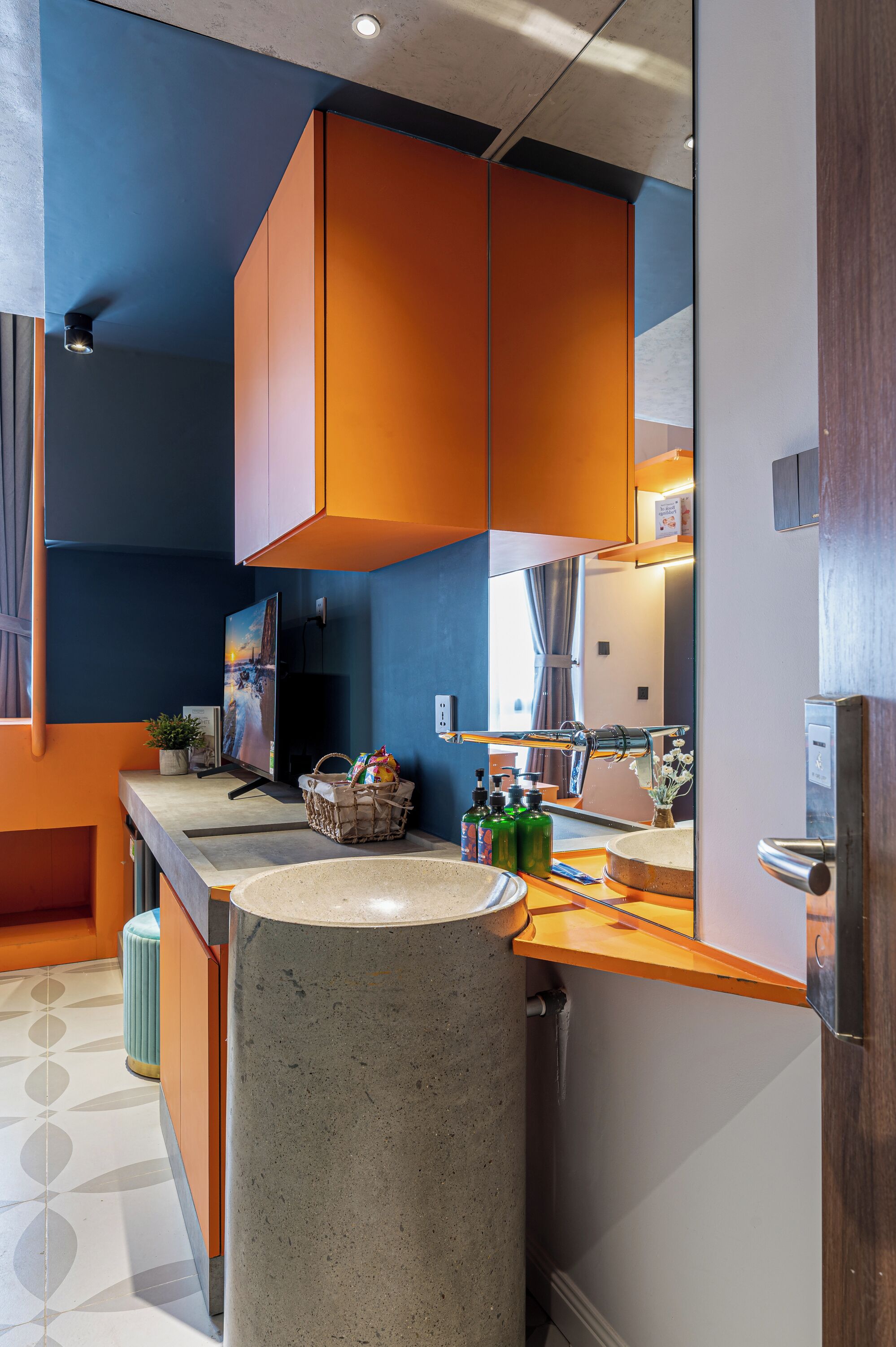 Un baño moderno con un espejo grande, un lavamanos de granito y muebles de color naranja.
