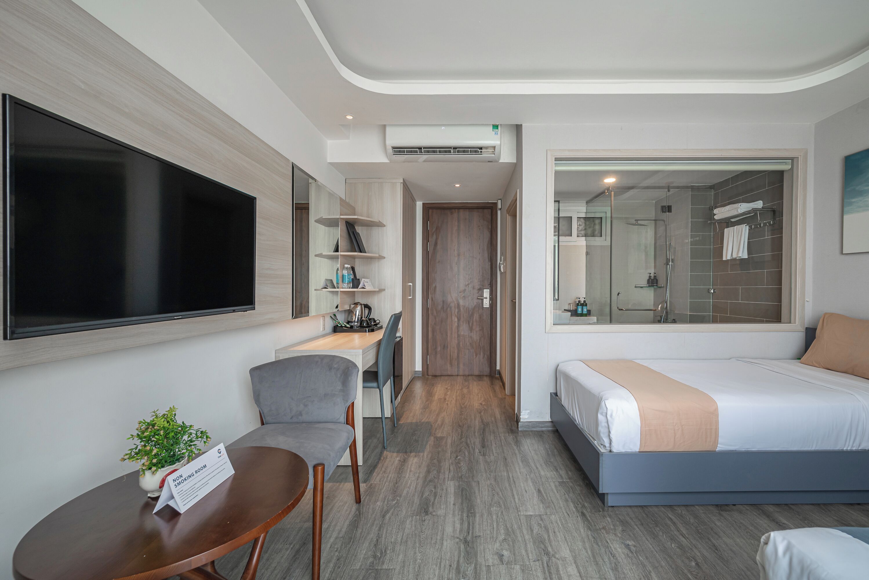 A hotel room with a bed, a desk, a chair, a TV, and a bathroom with a shower and toilet.