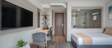 A hotel room with a bed, a desk, a chair, a TV, and a bathroom with a shower and toilet.