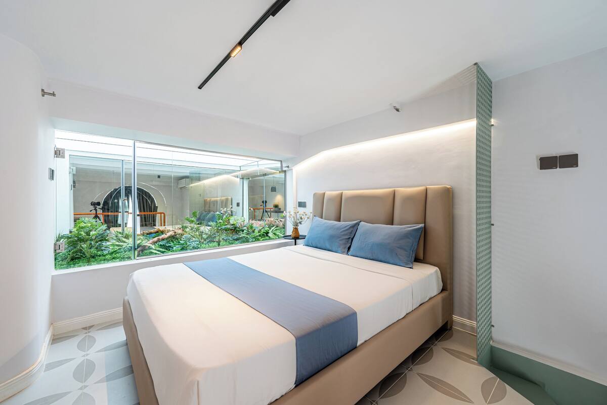 A modern bedroom with a large bed, a glass window, and a view of a garden.