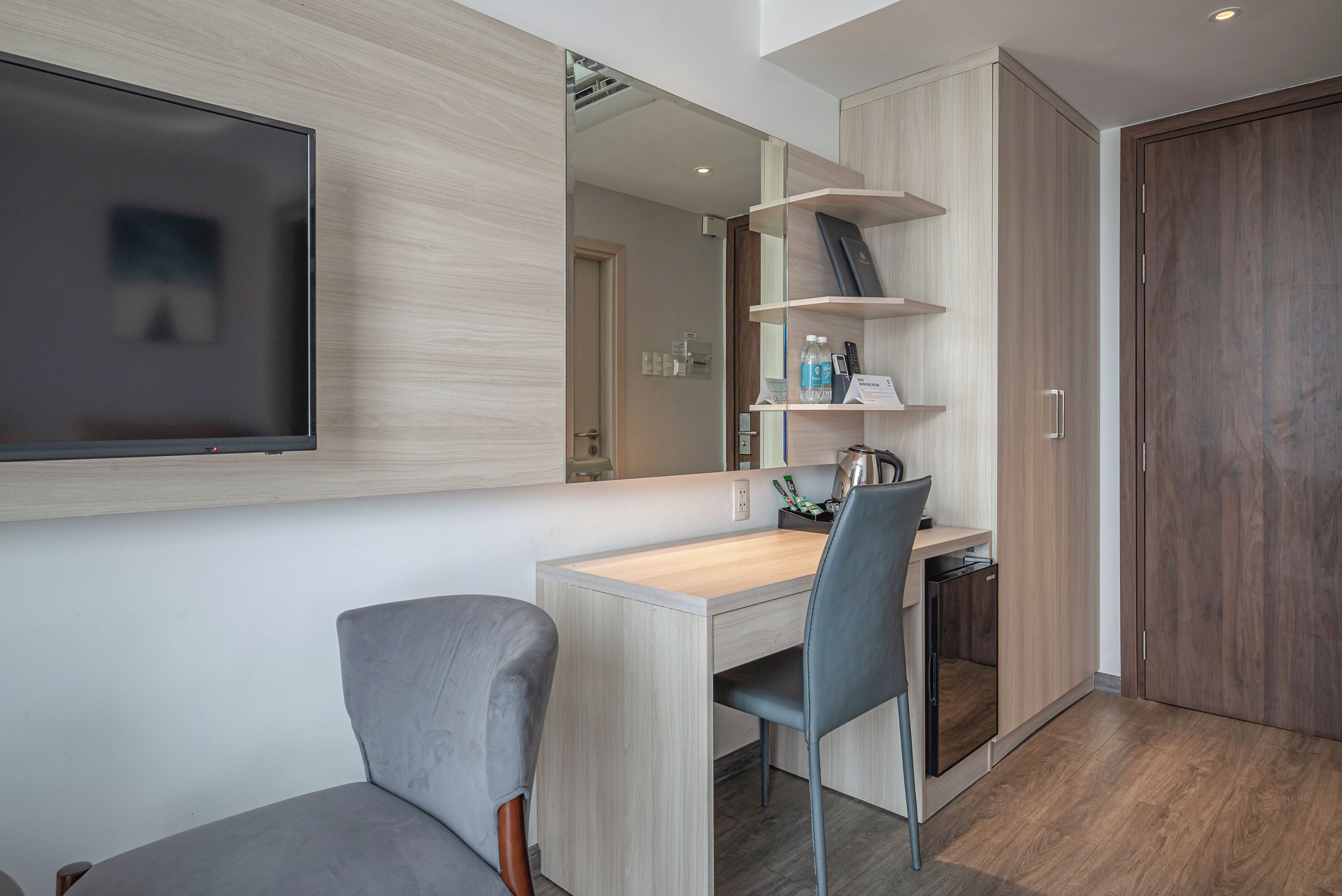 A modern room with a wooden desk, a grey chair, a flat-screen TV, and a wardrobe.