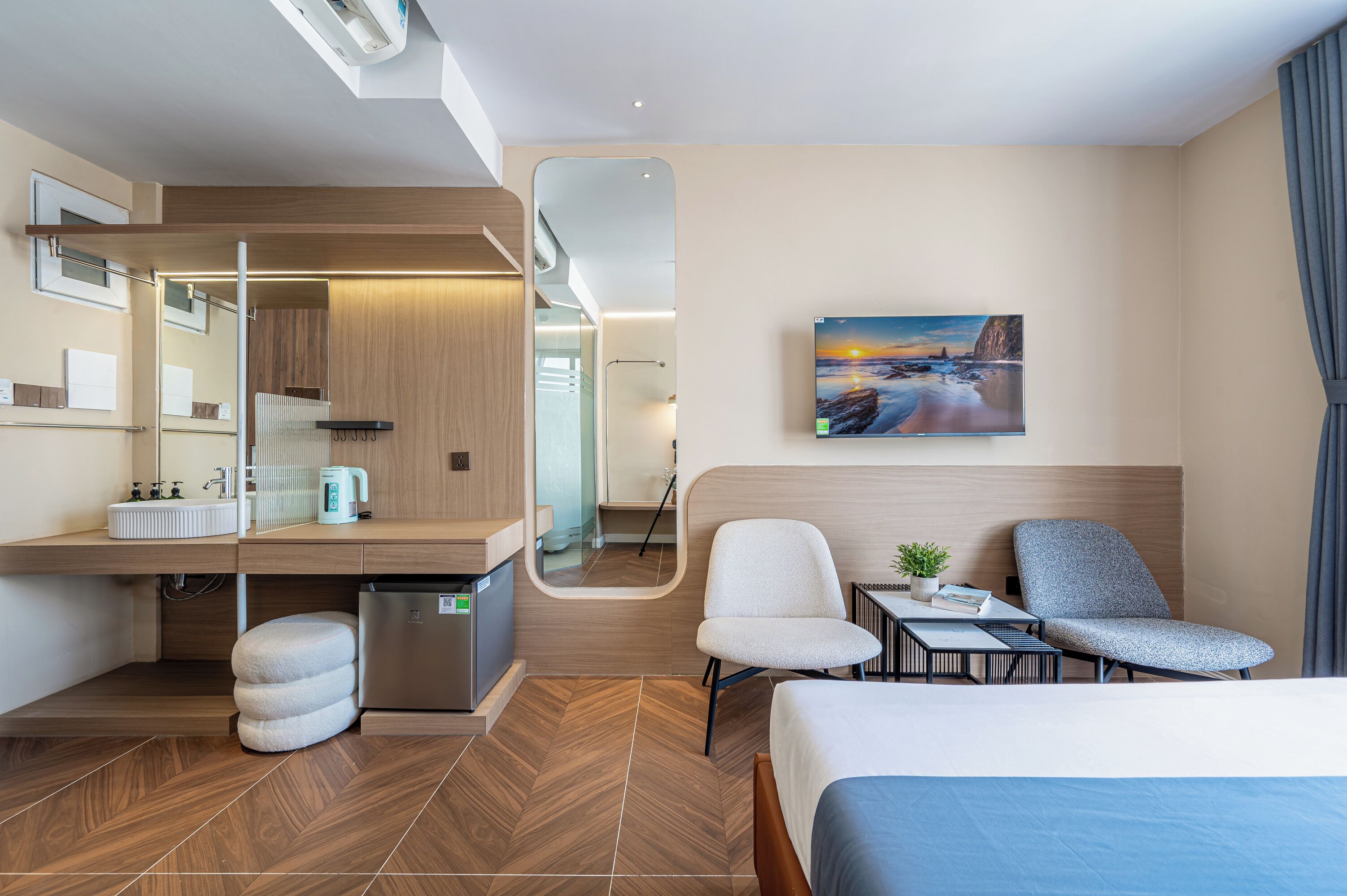 Moderni hotellihuone, jossa on sänky, työpöytä, tuoli ja pieni pöytä, jonka päällä on kasvi.