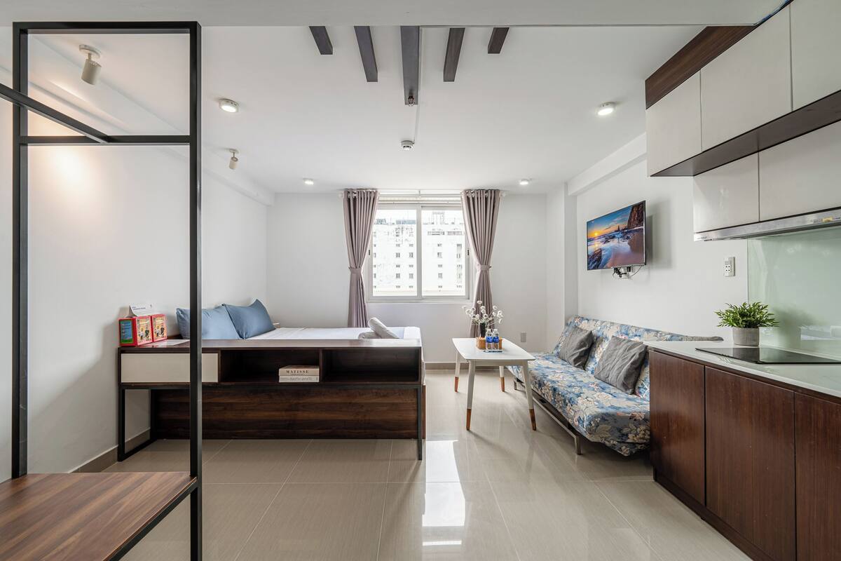 A modern apartment with a bed, sofa, dining table, and kitchen area.
