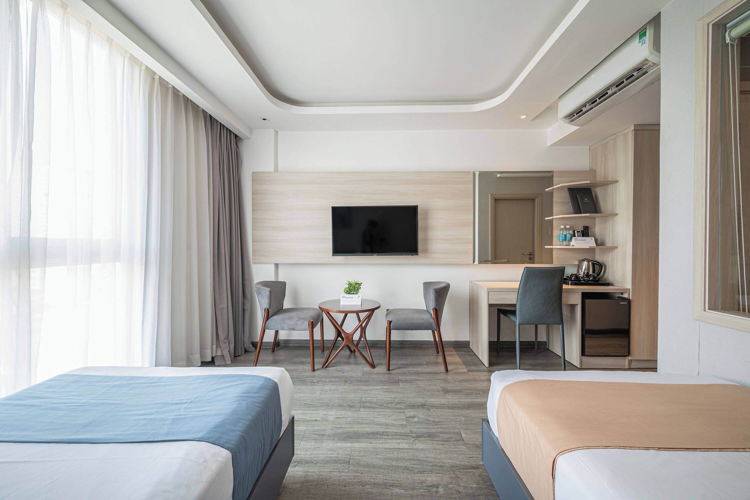 Ett modernt hotellrum med två sängar, ett skrivbord, en stol, en TV och ett litet pentry.