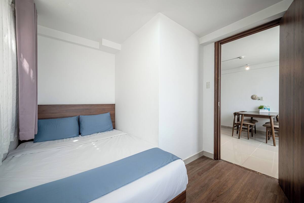 A bedroom with a bed, a wooden headboard, a blue blanket, and a wooden floor.