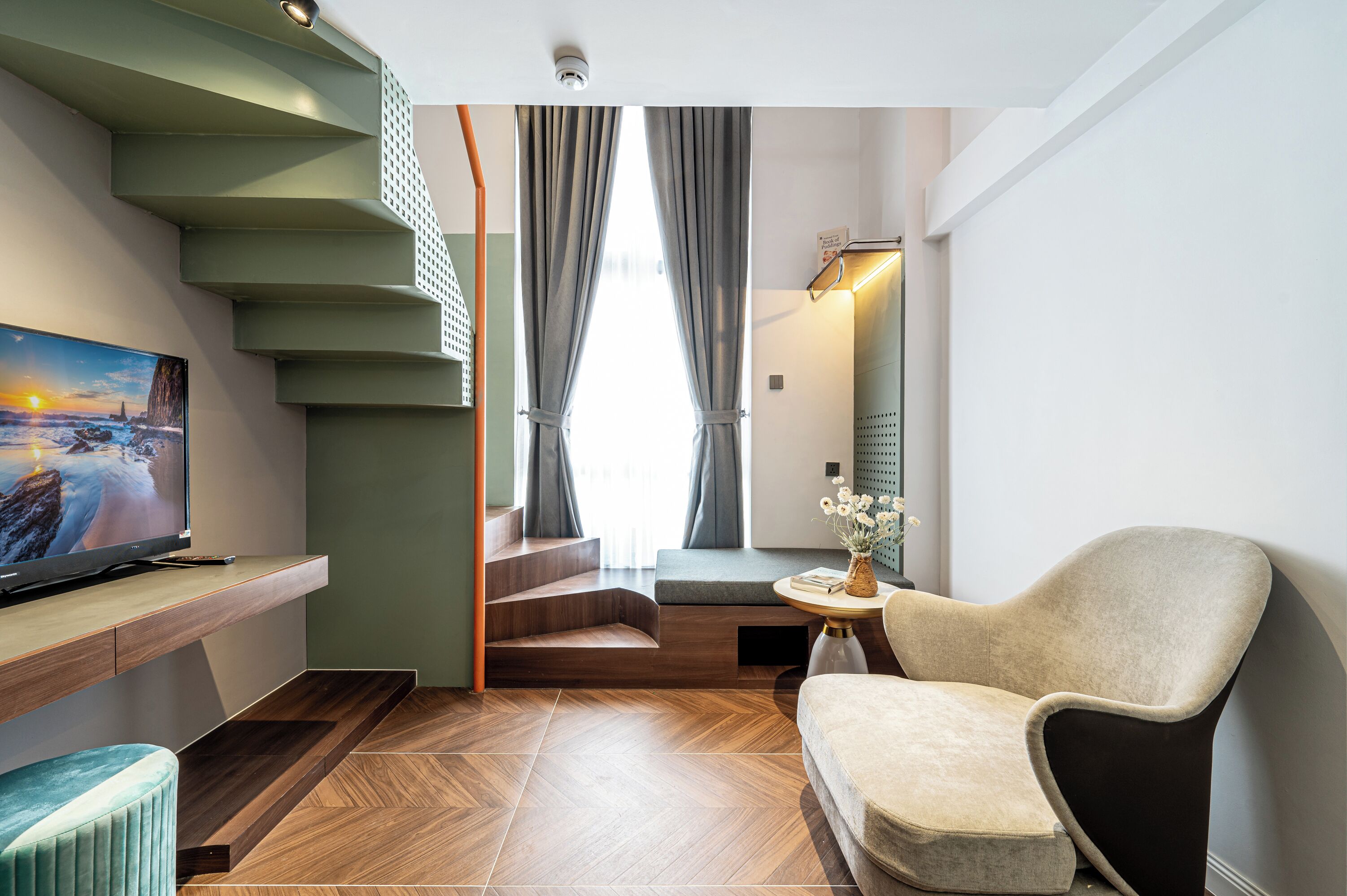 A modern living room with a staircase, a flat-screen TV, a sofa, and a small table with a vase.