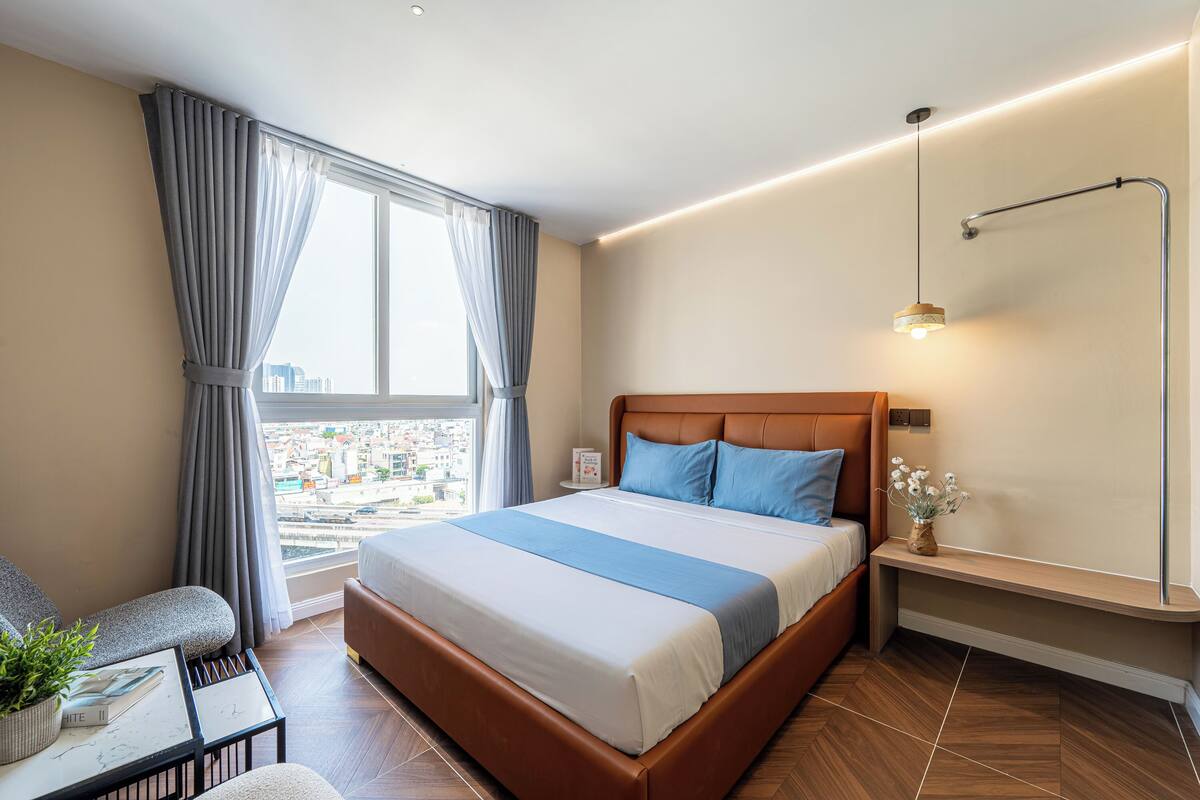 A modern hotel room with a large bed, a view of the city, a small table with a plant, and a bedside lamp.