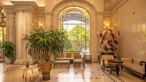 A spacious lobby with a large arched window, a sofa, chairs, a coffee table, and potted plants. - Cozrrum Lux - Sonata Imperial (Ho Chi Minh City)
