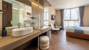 A modern hotel room with a large mirror, wooden vanity, a sofa bed, and a city view. - Cozrrum Lux - Sonata Imperial (Ho Chi Minh City)