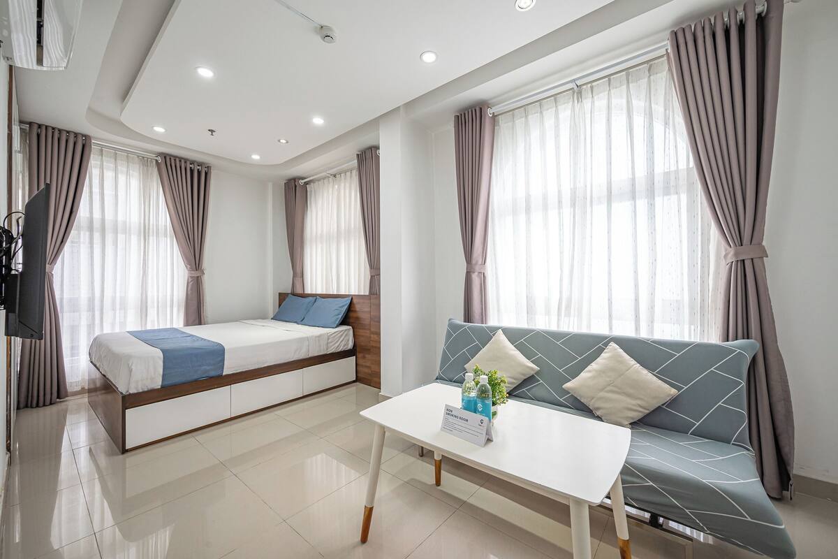 A modern hotel room with a bed, sofa, and a small table with amenities.