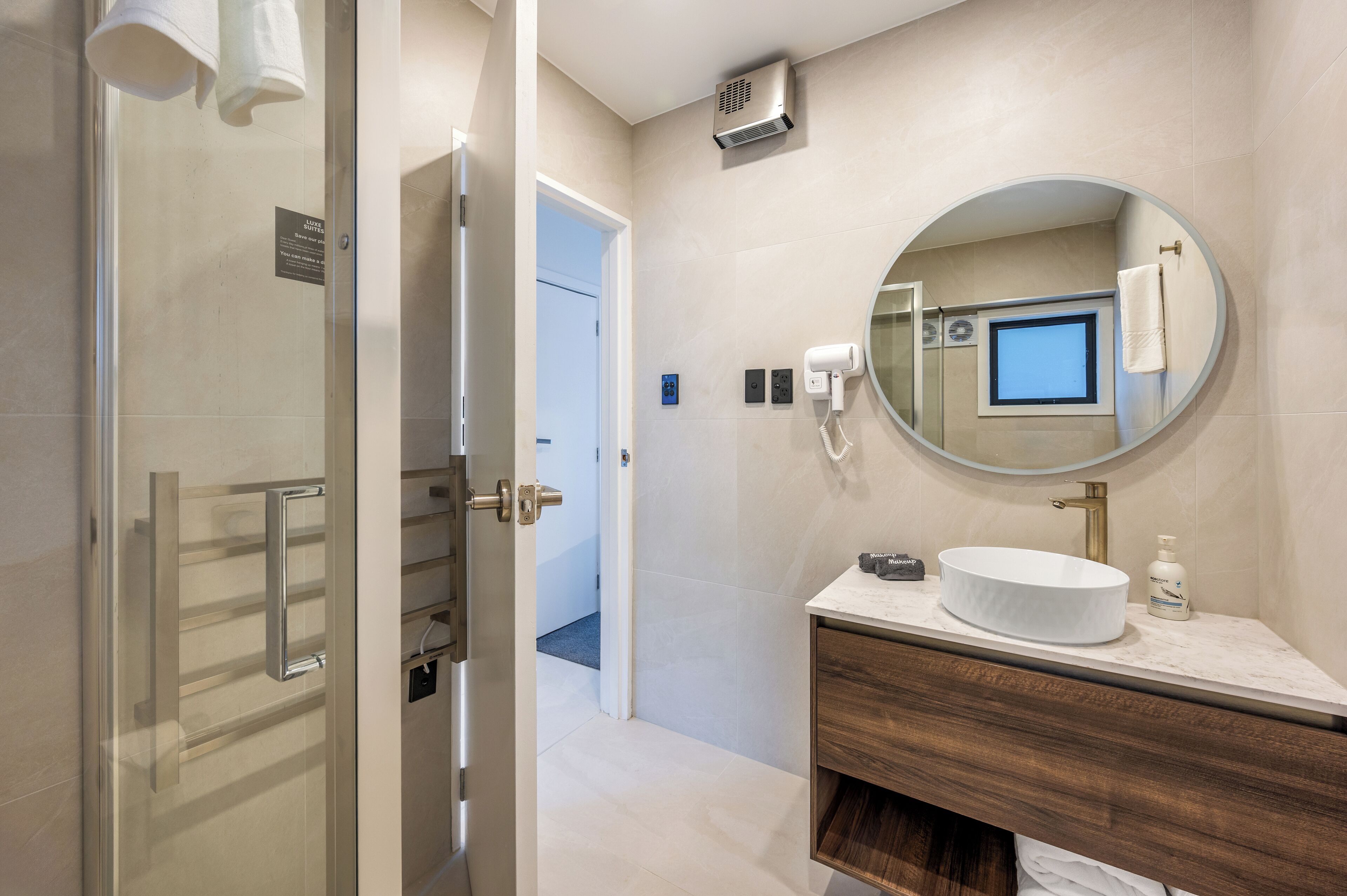 A modern bathroom with a glass shower door, a round mirror, a white sink, and a towel rack.