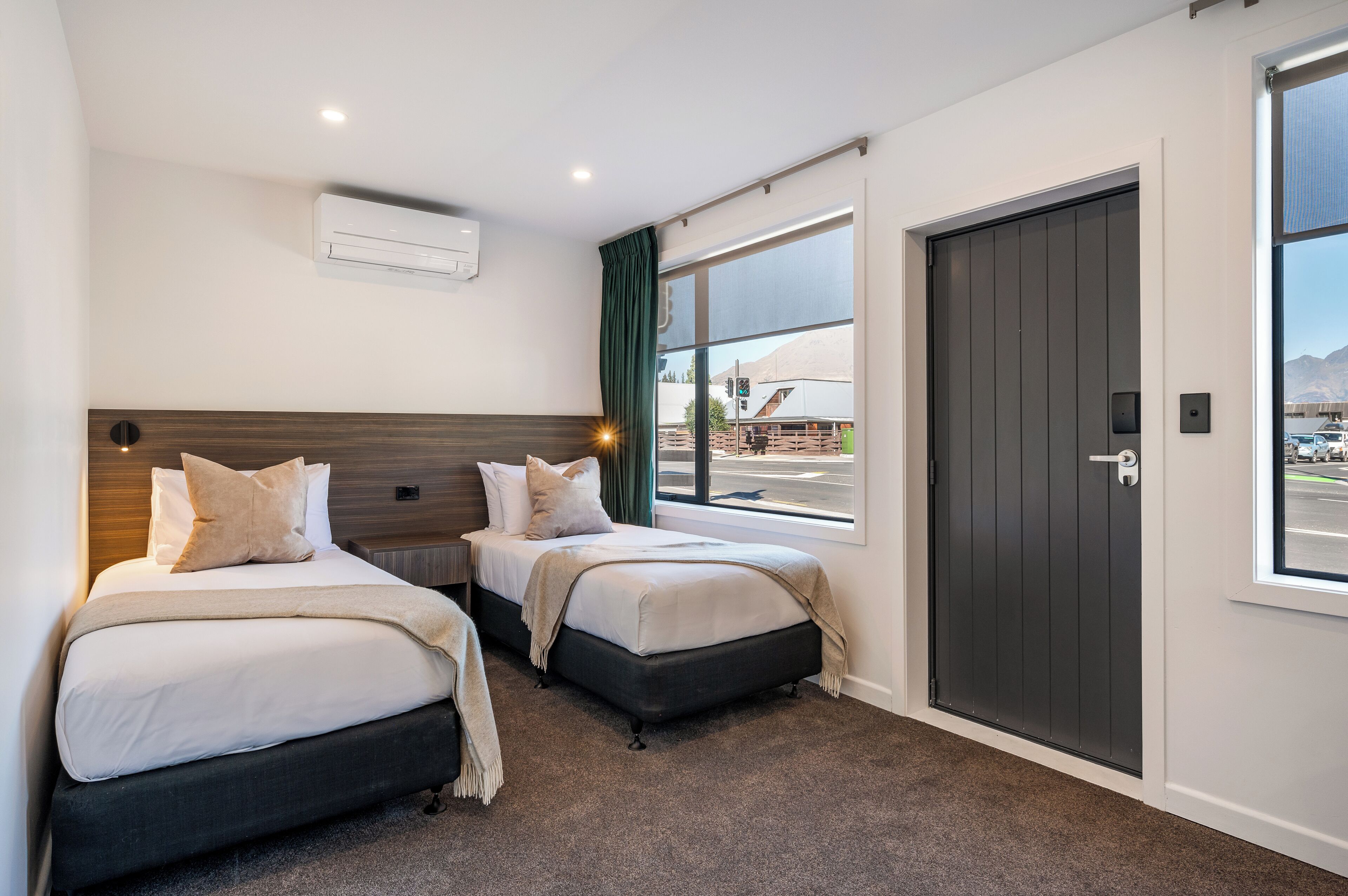 A hotel room with two beds, a large window, a door, and an air conditioning unit.