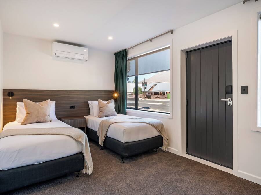 A hotel room with two beds, a large window, a door, and an air conditioning unit.