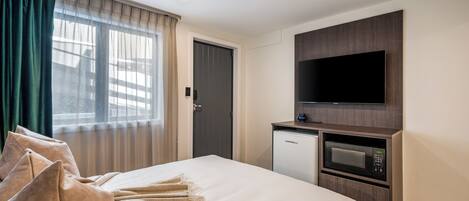A hotel room with a bed, a flat-screen TV mounted on a wooden panel, a mini-fridge, and a microwave.