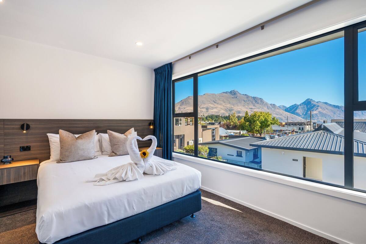 Una habitación de hotel moderna con una cama grande, vistas a montañas y al paisaje urbano.