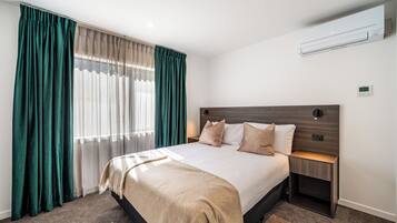 A hotel room with a large bed, a wooden headboard, a nightstand, and a wall-mounted air conditioner.