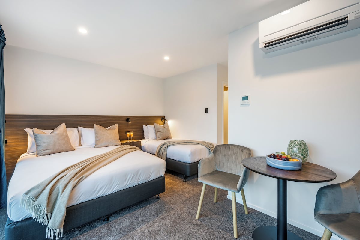 Habitación de hotel con dos camas, una mesita con un frutero, una silla y un equipo de aire acondicionado en la pared.