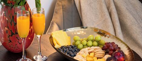 Ein Frühstücksbuffet mit Obstplatte, Käseplatte, zwei Orangensaftgläsern und einer Vase mit Blumen.