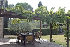 A covered outdoor dining area with a table and chairs, surrounded by greenery and a pergola. - My Exclusive Italy - Spacious Villa with Private Pool & Garden near Chianti (Impruneta)