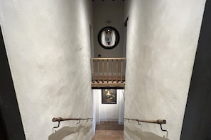 A narrow hallway with a wooden railing, a circular mirror on the wall, and a framed picture below the mirror.