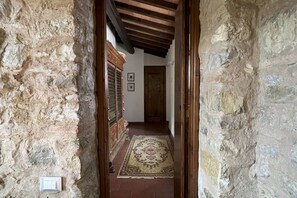 Un pasillo de paredes de piedra con una puerta de madera al final, un tapete estampado en el suelo y un interruptor de luz en la pared.
