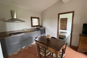 A kitchen with a gas stove, a stainless steel range hood, a window, and a dining area with a table and chairs. - My Exclusive Italy - Spacious Villa with Private Pool & Garden near Chianti (Impruneta)