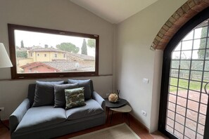 A room with a sofa, a small table, a lamp, and a view of buildings through a window. - My Exclusive Italy - Spacious Villa with Private Pool & Garden near Chianti (Impruneta)