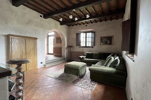 Una sala de estar con un sofá verde, un mueble de madera, un tapete estampado y un techo con vigas a la vista.