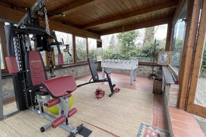 A covered gym area with exercise equipment, a foosball table, and a window overlooking a garden. - My Exclusive Italy - Spacious Villa with Private Pool & Garden near Chianti (Impruneta)