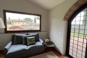 A room with a sofa, a small table, a lamp, and a view of buildings through a window. - My Exclusive Italy - Spacious Villa with Private Pool & Garden near Chianti (Impruneta)