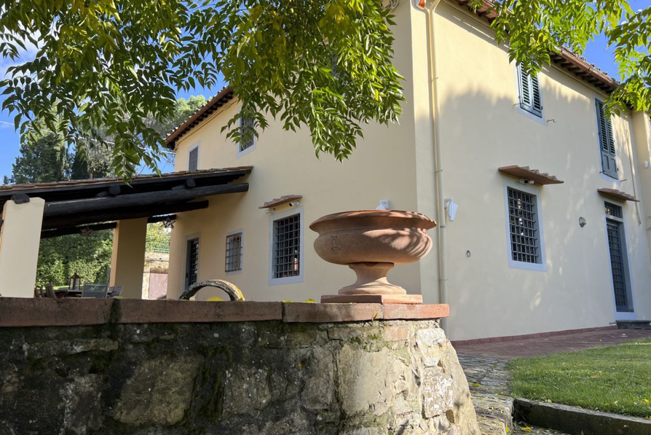 Un edificio con pared de piedra, una maceta grande de terracota y una pérgola.