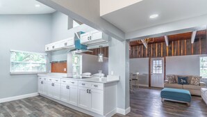 Una cocina moderna con armarios blancos, una isla central y una zona de comedor con sofá y reposapiés.