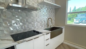 Cuina moderna amb taulell blanc, rentamicroones d'acer inoxidable i un mosaic original al mur.