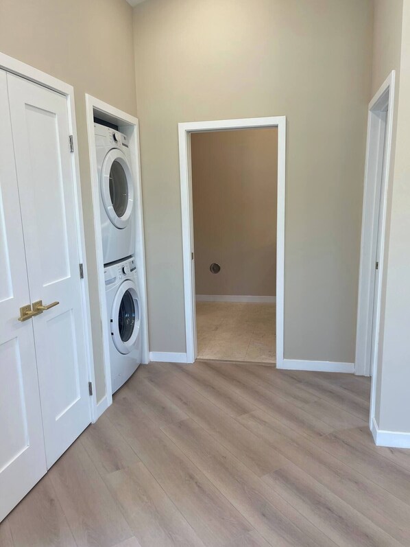 A laundry room with a front-loading washer and dryer, wooden flooring, and white walls.