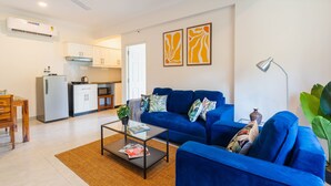 A modern living room with a blue sofa, a coffee table, and a dining area with a wooden table and chairs. - Mona Collective at Serenova (Calangute)