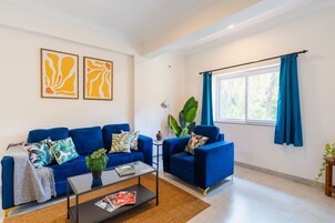Una sala de estar con un sofá azul, una mesita de centro y dos cuadros abstractos en la pared.