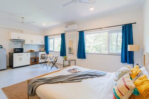 Habitación de hotel moderna con una cama grande, una pequeña kitchenette, un área de comedor y vistas al exterior.